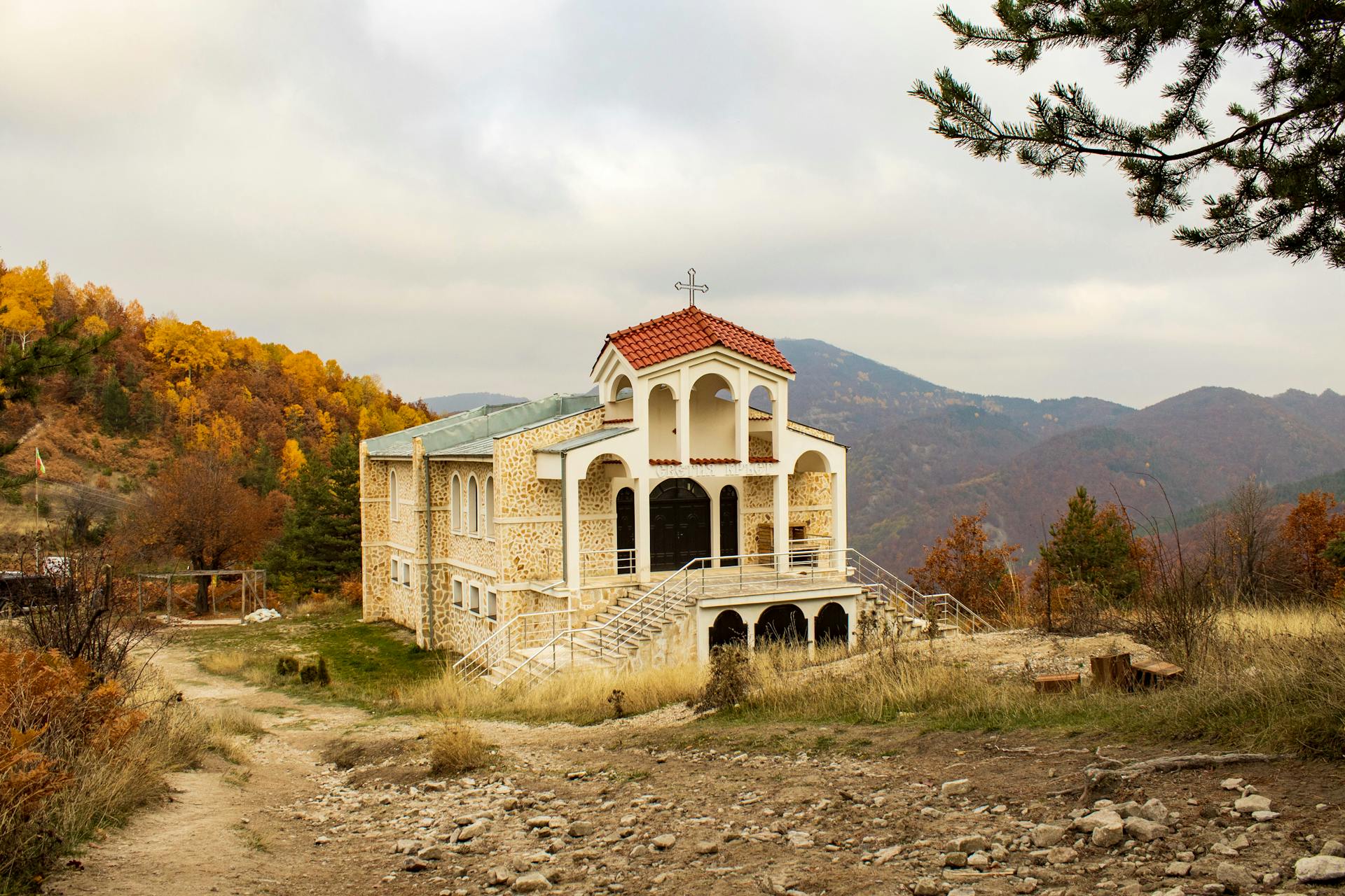 Picturesque chapel in a rural autumn landscape surrounded by hills and vibrant foliage.