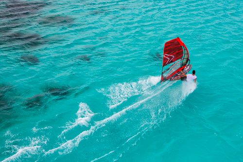 Free Aerial view of a man windsurfing on vibrant turquoise waters in Australia. Adventure and excitement captured in a stunning setting. Stock Photo