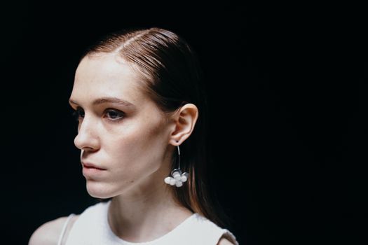 Portrait of a young woman with a floral earring against a dark background.