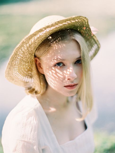 Beautiful blonde woman wearing a hat, captured in sunlight in a garden setting.
