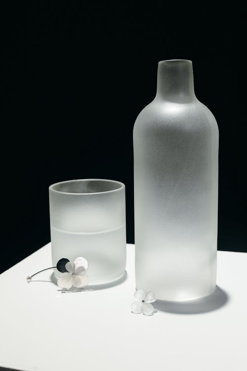 Drinking Glass with Water and Bottle on White Surface