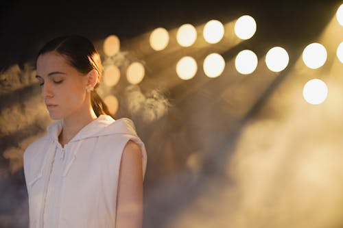 Young Woman Standing with Eyes Closed on the Background of Stage Lights and Smoke 