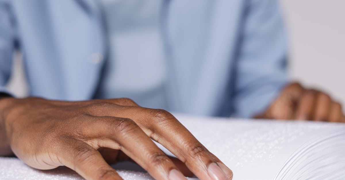 A close-up shot of an adult's hand reading braille on an open book, indicating a focus on accessibility.