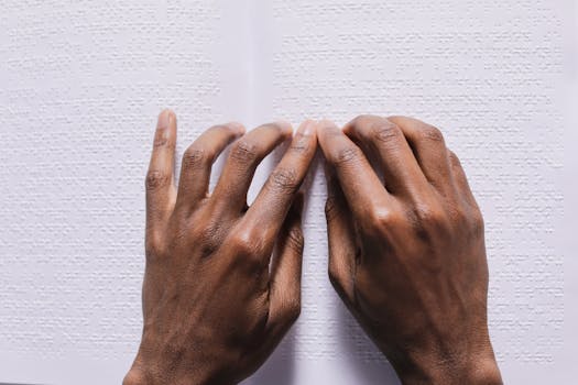 Close-up of hands reading a Braille book on a white background, illustrating tactile reading skills.