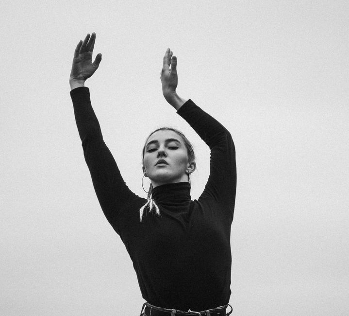Black and white portrait of a woman in a black turtleneck with arms raised gracefully.
