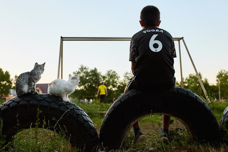 A Boy Sitting On Rubber Tire Watching A Football Game