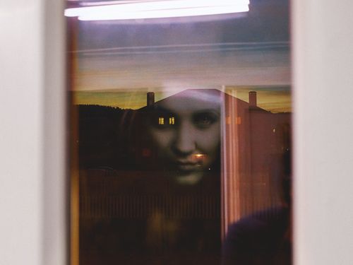 Free A haunting reflection of a woman's face appears in the window at twilight. Stock Photo