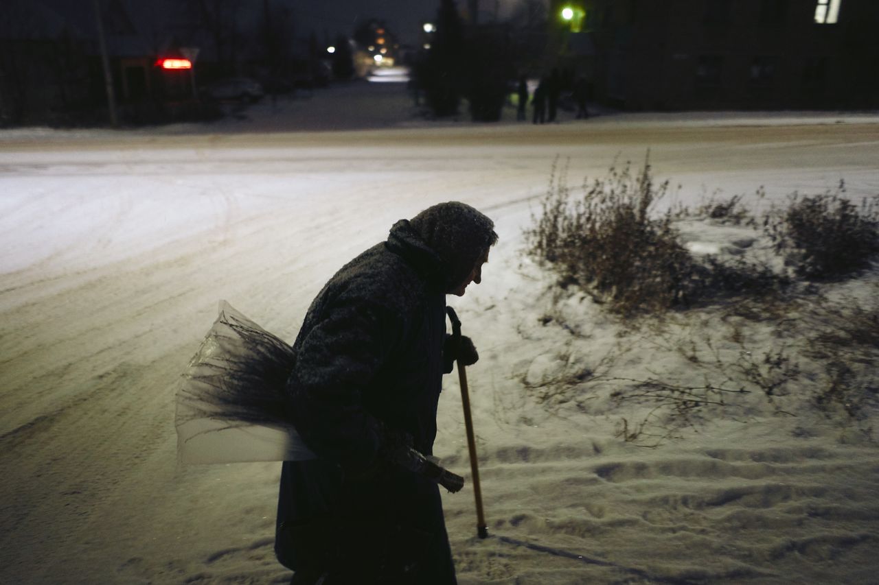 Silhouette of an elderly woman with a cane walking in snow at night