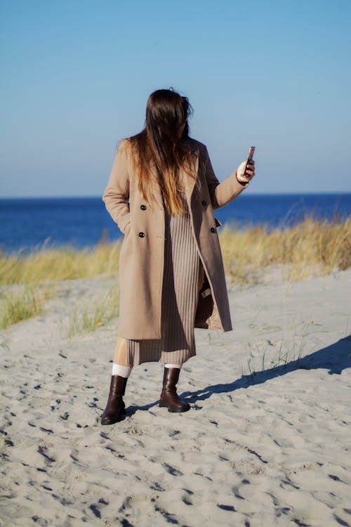Woman in Brown Coat Standing on White Sand