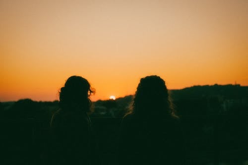A Silhouette of Two People Looking at Sunset 