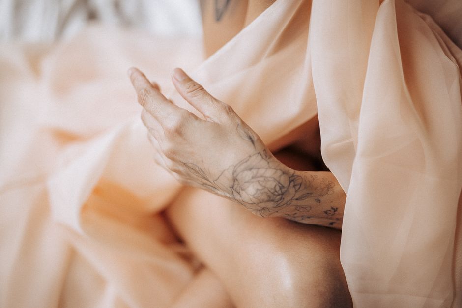 Close-up of a tattooed hand gracefully posed with sheer fabric, evoking elegance and artistry.