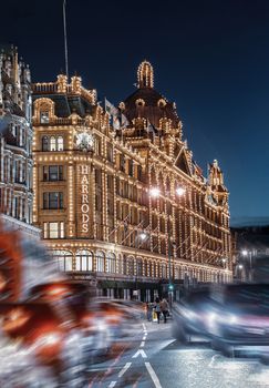 Harrods department store in London at night, beautifully lit with vibrant city life around.