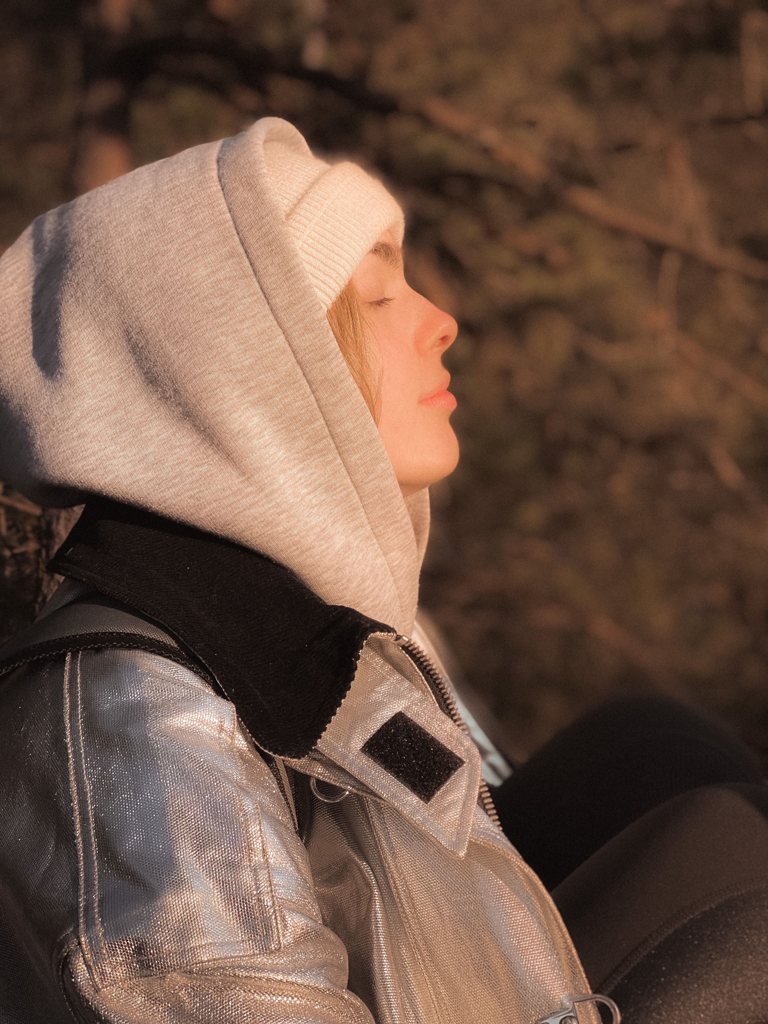 Side view portrait of a woman in a hoodie and beanie enjoying the outdoors with eyes closed.