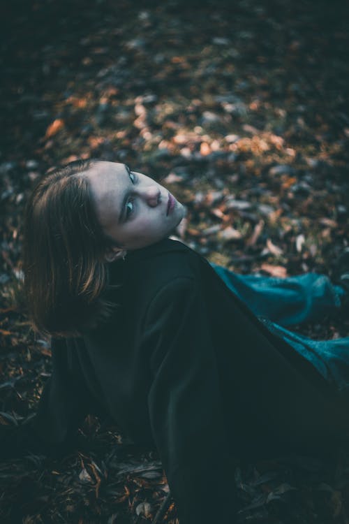 Woman in Black Long Sleeve Shirt Sitting on Ground With Dried Leaves