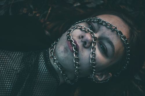 Free Close-up artistic portrait of a woman wrapped in chains lying outdoors, conveying a dramatic and mysterious atmosphere. Stock Photo