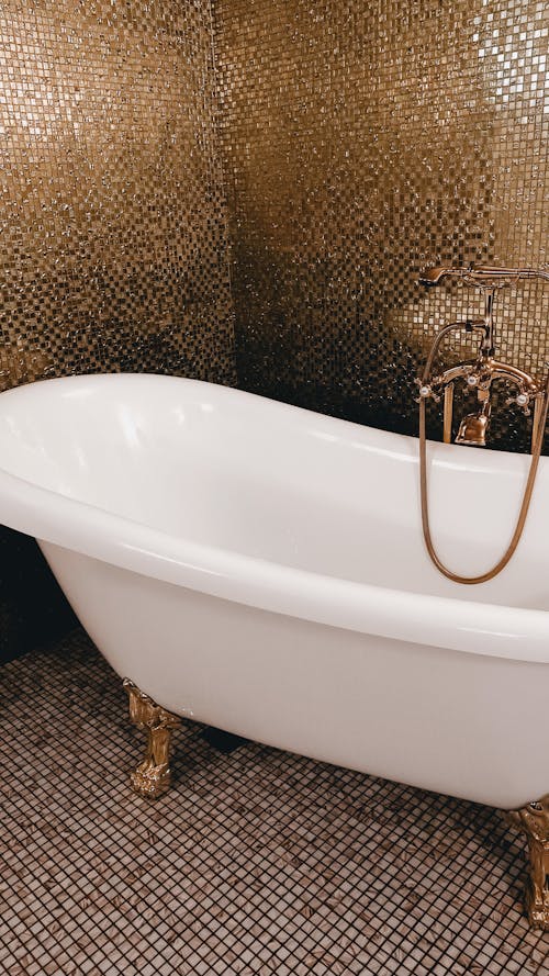 White Bath Tub near Gold Mosaic Tiles