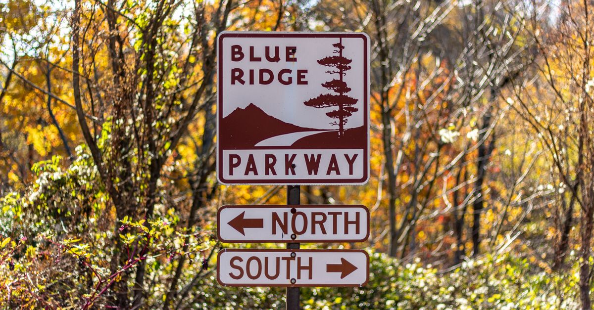 A directional sign on Blue Ridge Parkway with vibrant autumn leaves in Cherokee, NC.