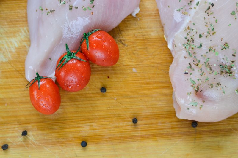 Fresh raw chicken with cherry tomatoes on a wooden board