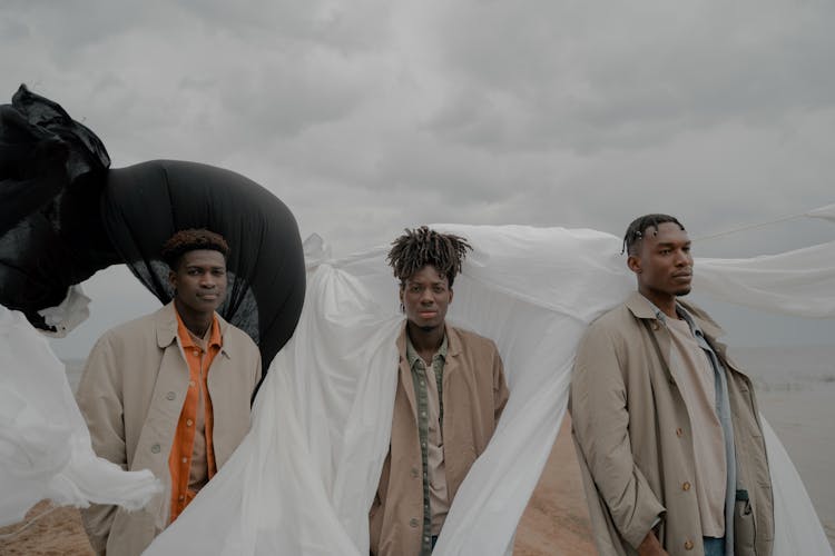 Men In Coats Standing On Beach With White And Black Cloth In Wind