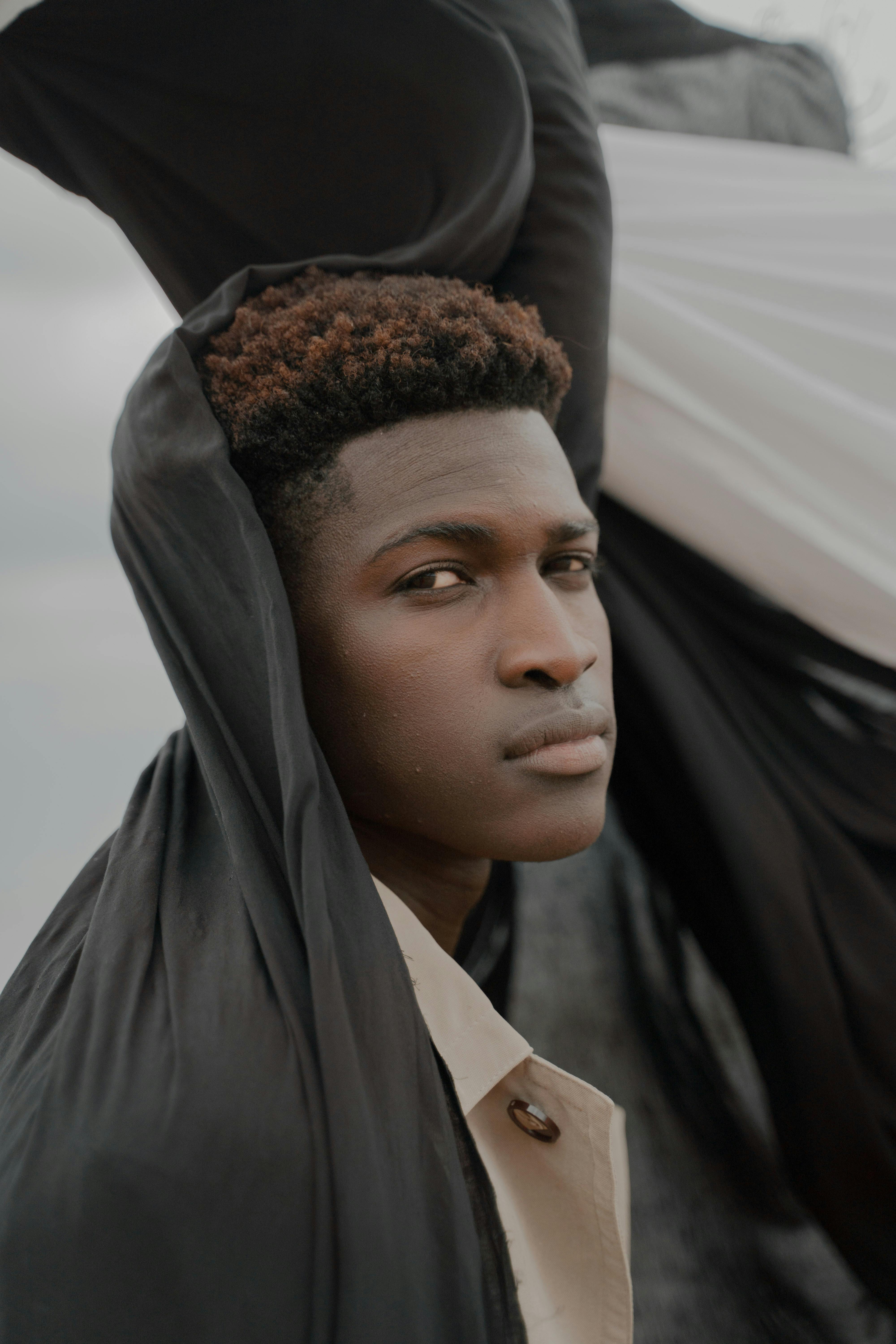 Artistic portrait of a young black man wrapped in flowing fabric with a somber expression.