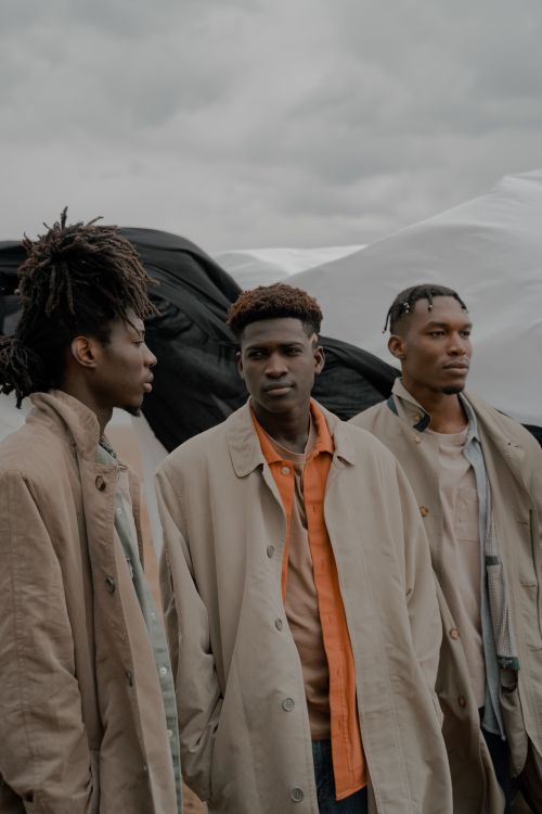 Free Three African men in beige coats posing outdoors with a minimalistic background. Stock Photo