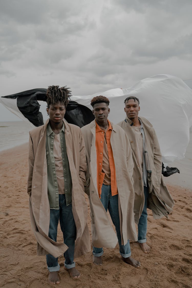 Men In Coats Standing On Beach With White And Black Cloth In Wind