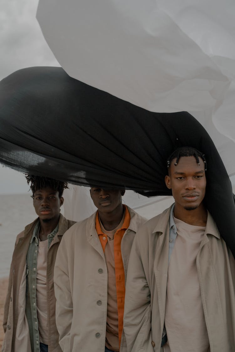 Men In Coats Standing On Beach With White And Black Cloth In Wind