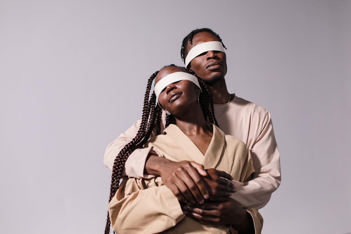 Man in Beige Long Sleeves Shirt Hugging Woman Wearing Brown Coat Blindfolded