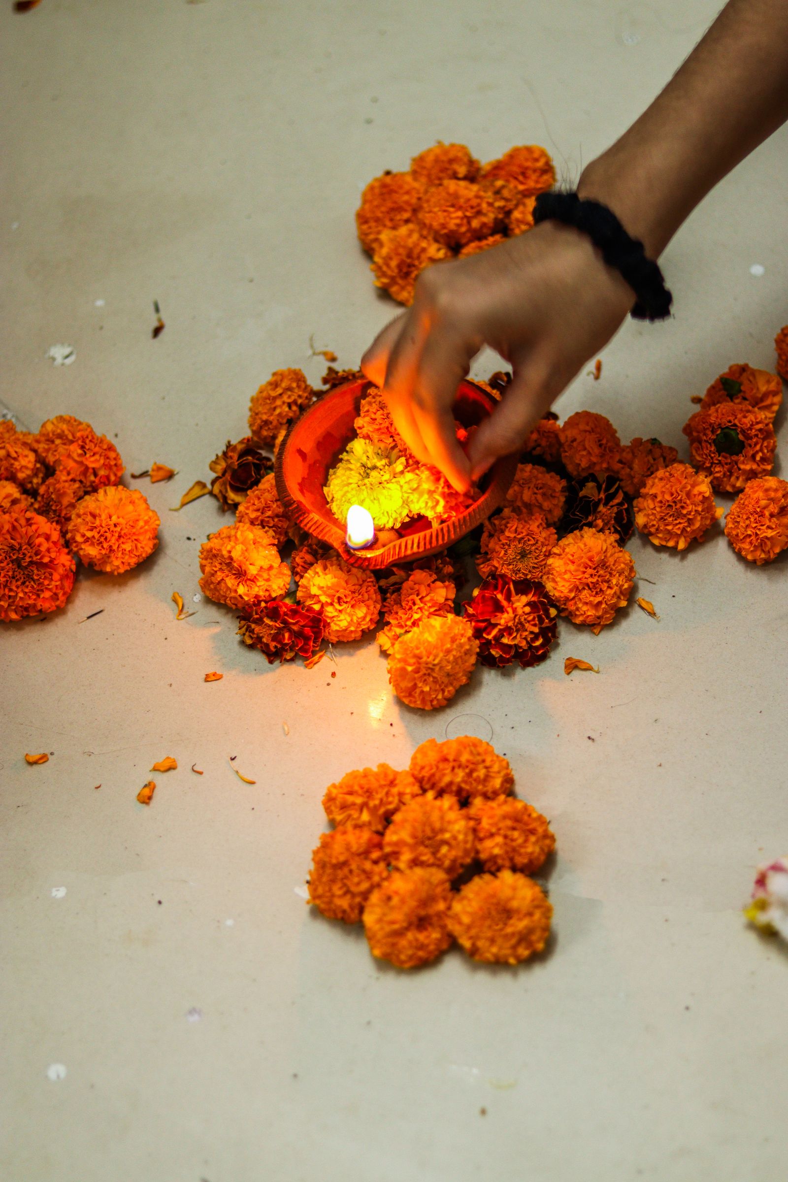 A hand lighting a small clay lamp set among scattered marigold flowers during Tihar