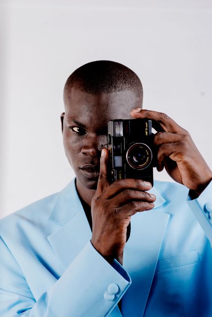 Portrait of an African man in a blue suit holding a vintage camera.