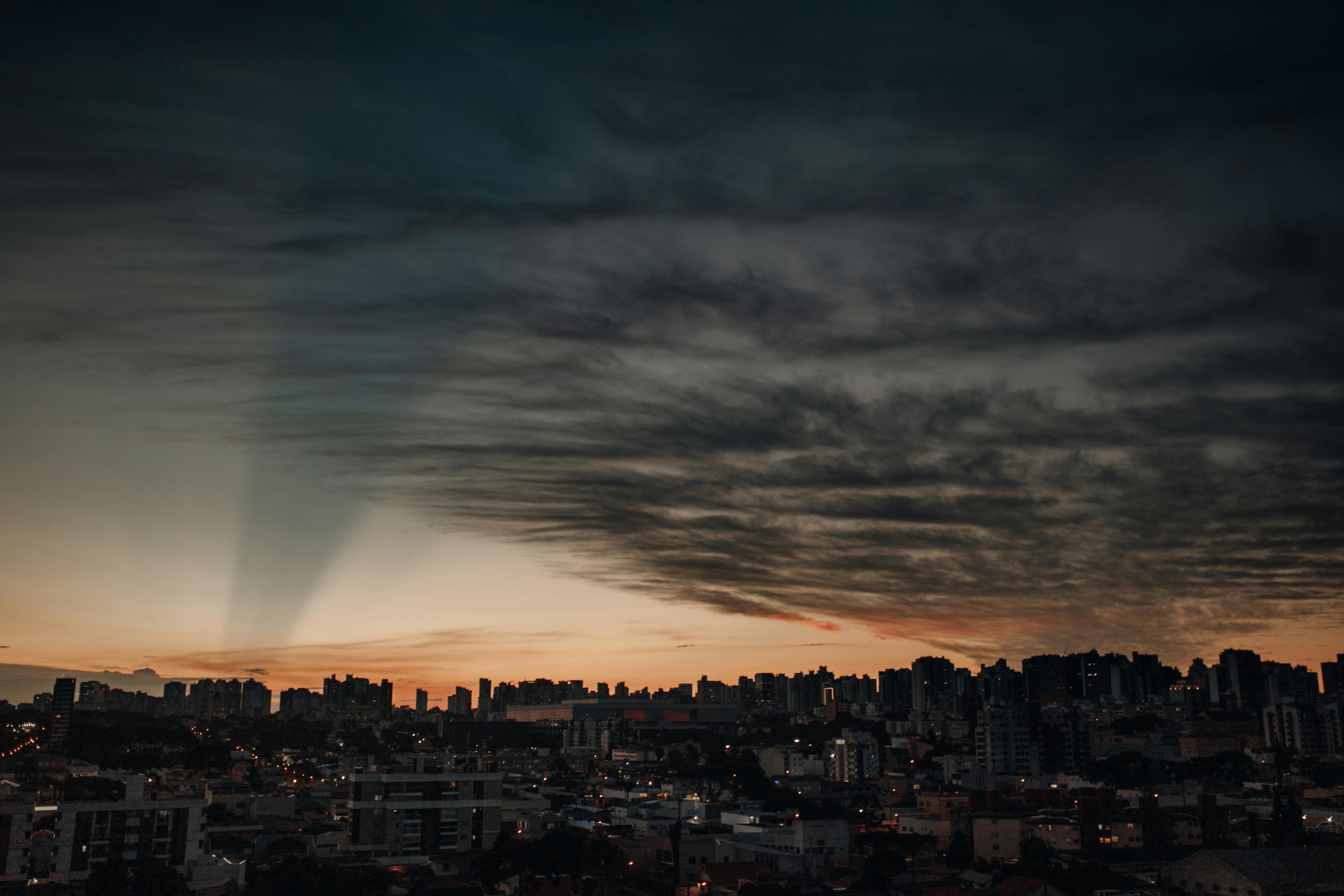 A breathtaking view of Curitiba skyline illuminated under a vibrant sunset sky with dramatic clouds.