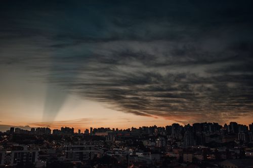 Free A breathtaking view of Curitiba skyline illuminated under a vibrant sunset sky with dramatic clouds. Stock Photo