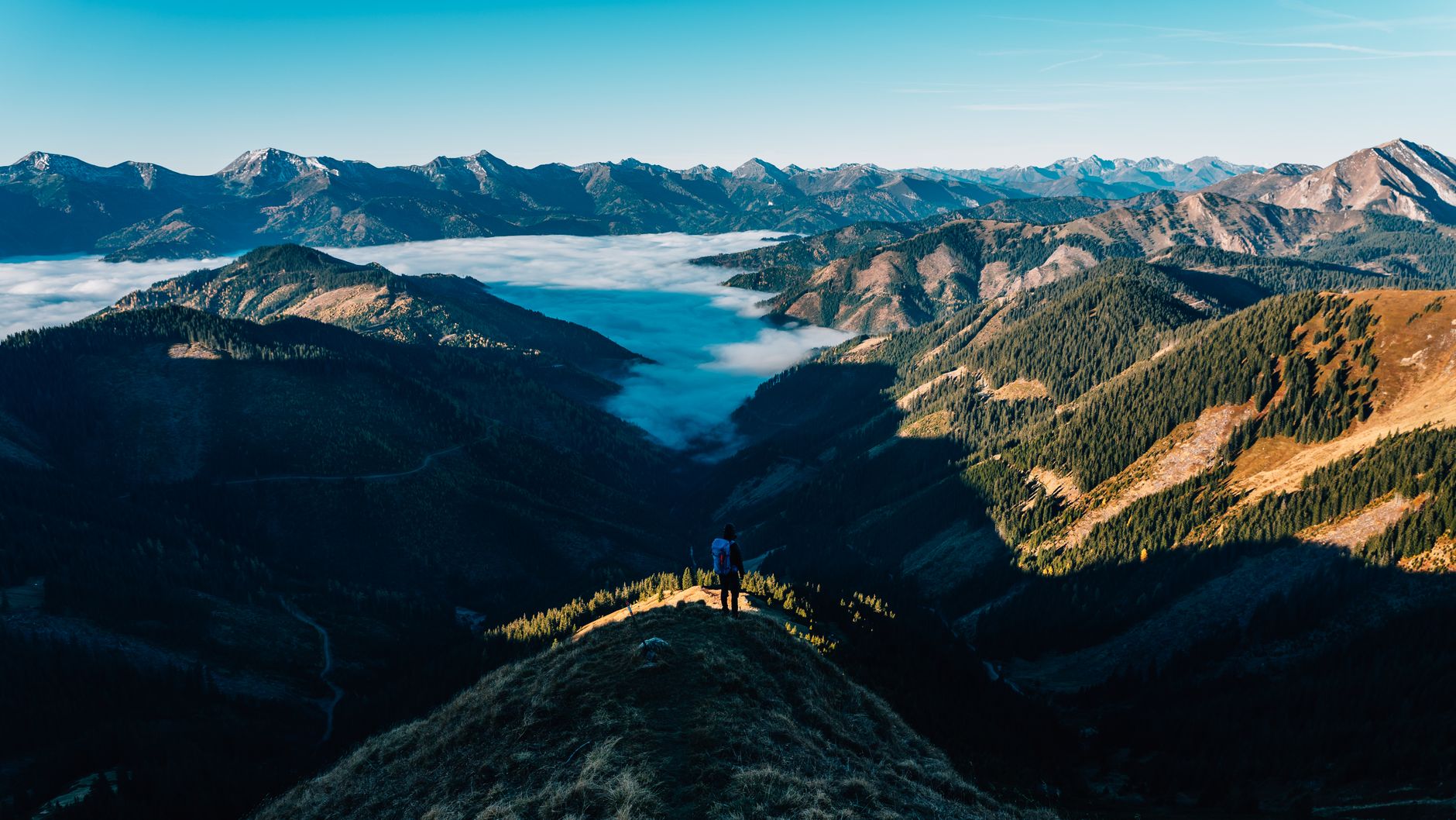 A tranquil scene of a lone hiker standing atop a mountain peak, overlooking vast mountain ranges at sunrise.