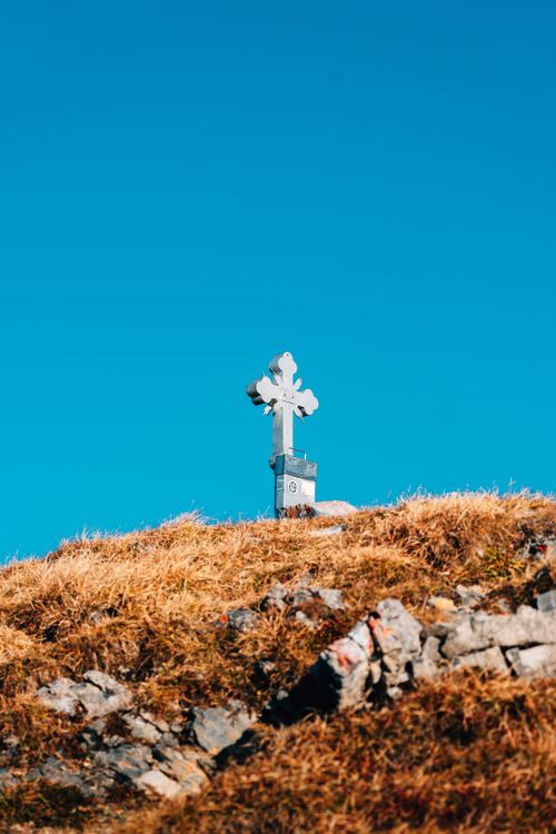 Free A lone cross stands atop a hill with a clear blue sky backdrop, conveying solitude and serenity. Stock Photo