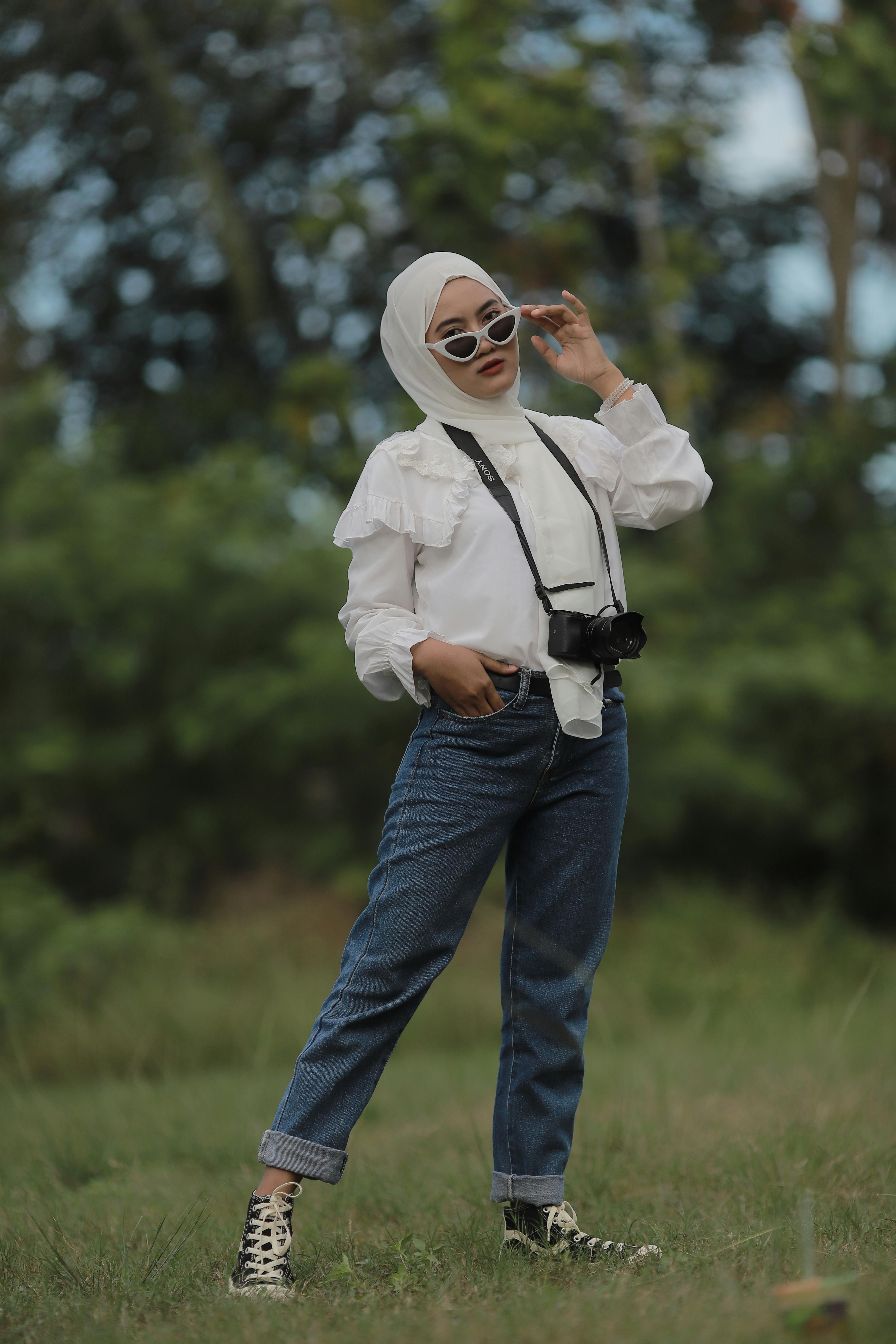 Stylish woman in hijab and sunglasses poses with a camera in nature.
