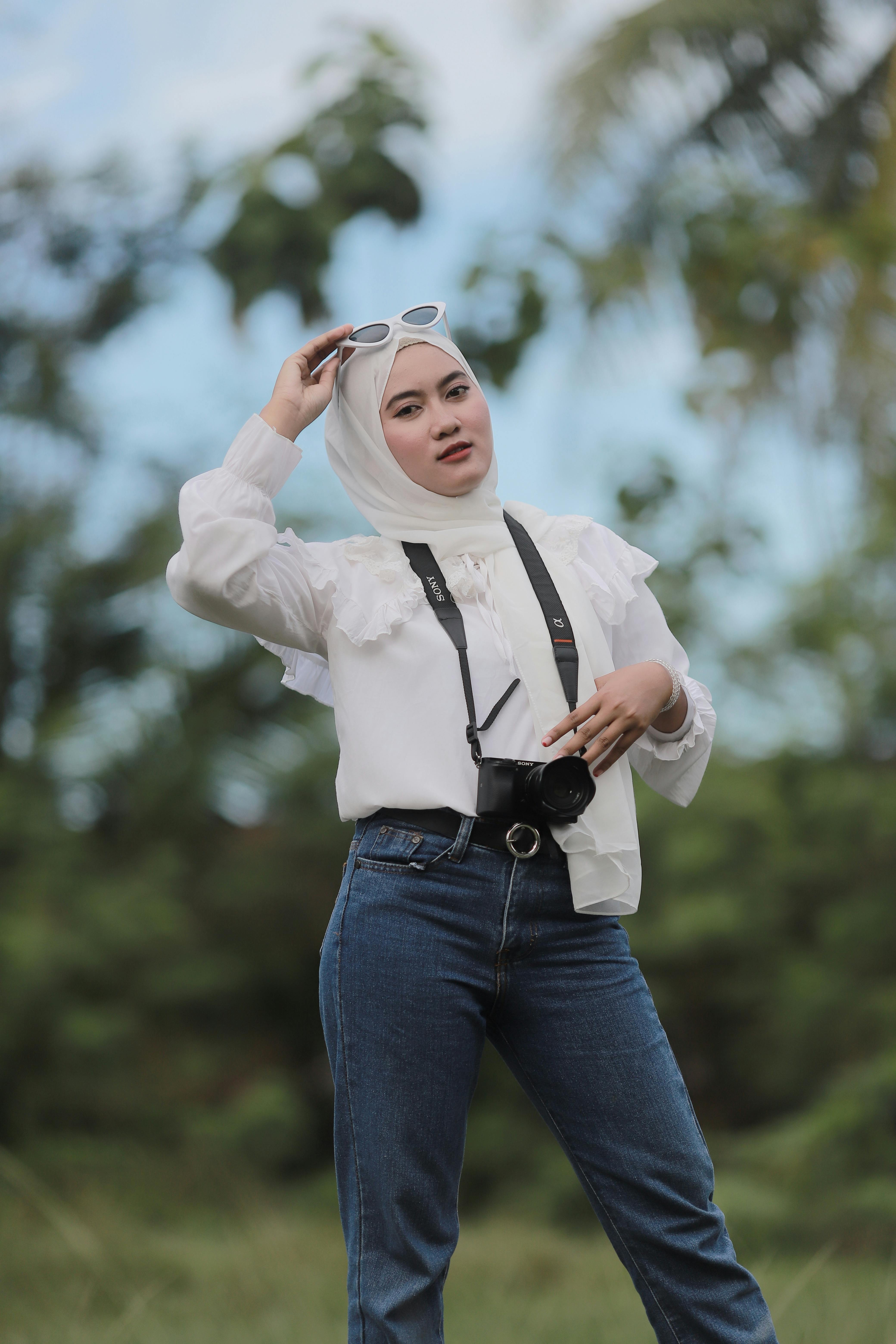 Chic Muslim woman in hijab posing confidently with a camera outdoors in nature.