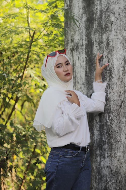 Woman in White Long Sleeve Shirt and Blue Denim Jeans Standing Beside Tree
