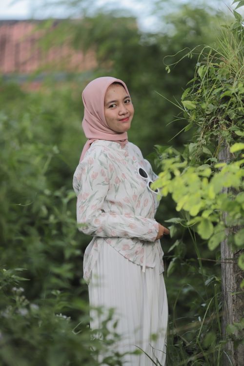 Free A smiling woman in a hijab poses amidst greenery, showcasing a serene outdoor setting. Stock Photo