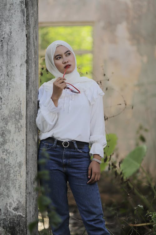 Woman in White Dress Shirt and Blue Denim Jeans Standing Beside Concrete Wall