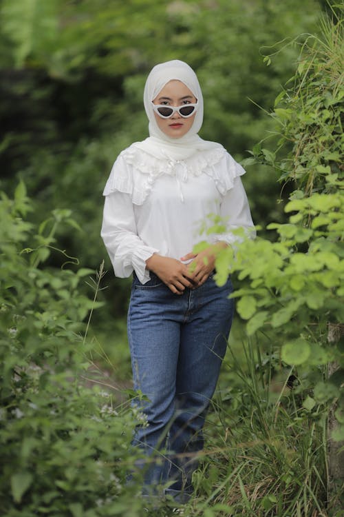 Free Woman in White Long Sleeve Shirt and Blue Denim Jeans Wearing White Sunglasses Stock Photo