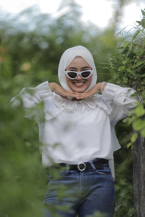 Free A cheerful Muslim woman in a hijab poses playfully outdoors, surrounded by greenery. Stock Photo