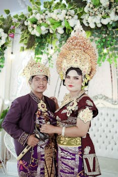 A couple in traditional Balinese attire during a wedding ceremony indoors with floral decor.