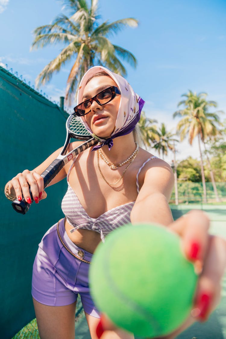 Woman Holding Up Tennis Ball To Camera