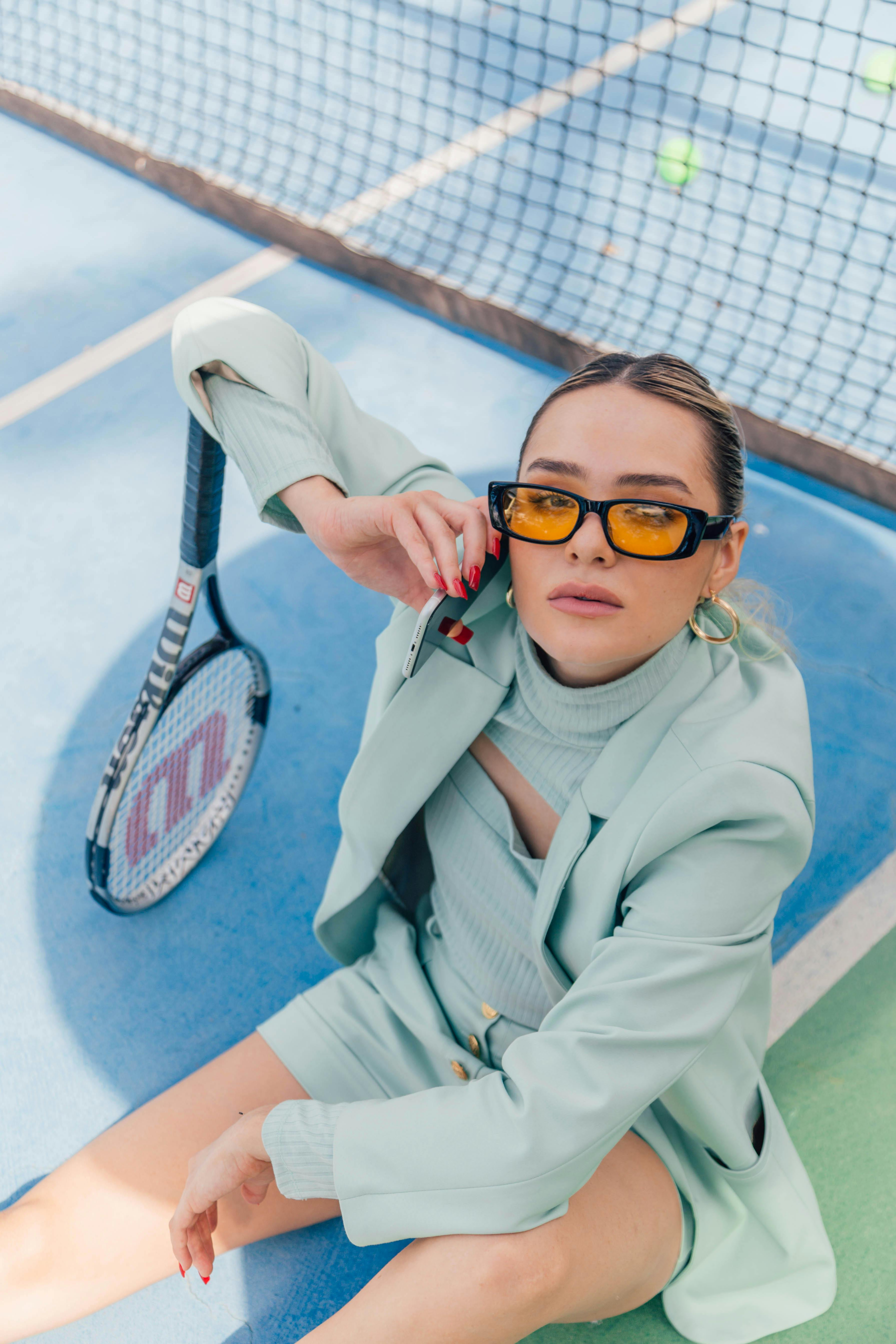 Fashionable woman in a mint suit poses with tennis racket on court.