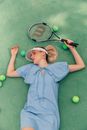 Woman in Blue Dress Laying on Ground Holding Racket Surrounded by Tennis Balls 