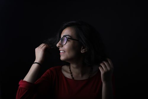 Free Profile of a young woman with eyeglasses smiling in a dark studio setting. Stock Photo