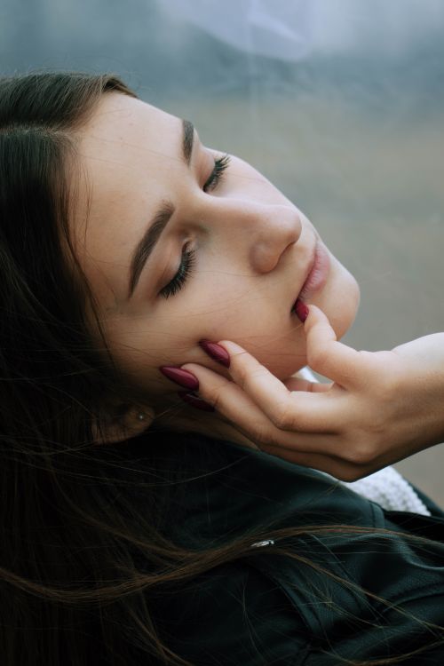 Free A young woman with closed eyes gently touching her face, embodying pensive relaxation. Stock Photo
