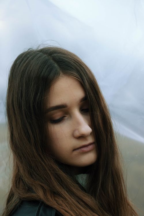 Free A tranquil portrait of a girl with long brown hair and eyes closed against a misty backdrop. Stock Photo