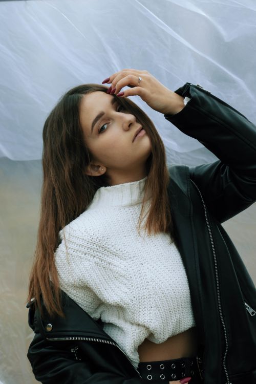 Free Young woman with brunette hair wearing a trendy white sweater and black jacket, looking fashionable outdoors. Stock Photo