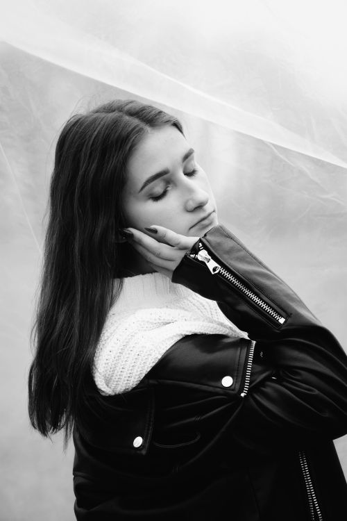 Free Emotive black and white portrait of a woman in a stylish leather jacket with closed eyes. Stock Photo